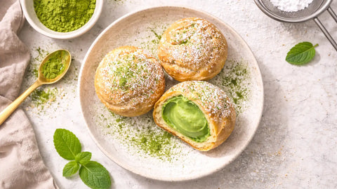 Plate of matcha cream puffs with green filling and powdered sugar on top