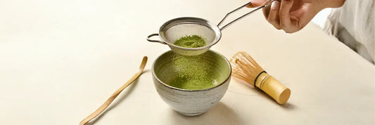Matcha powder being sifted through a fine mesh into a chawan before whisking.