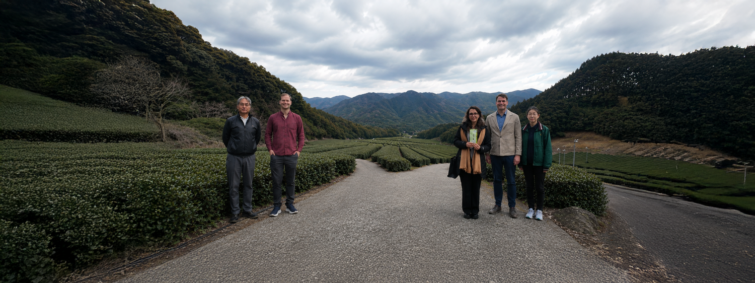 Nio Teas team with Will Klingner, Oliver Staerkle, and the Sato family at a Japanese tea plantation with mountains in the background.
